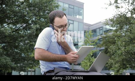 Business man using tablet and laptop while talking on smartphone Stock Photo