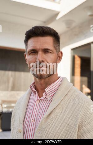 Vertical portrait of handsome mature man looking at camera while standing at outdoor terrace Stock Photo