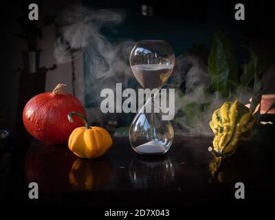 Halloween time countdown modern hourglass against a blurry background from the window - sand seeping through the bubbles of the crystal hourglass. Smo Stock Photo
