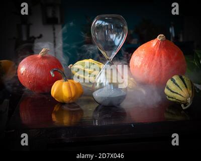 Halloween time countdown modern hourglass against a blurry background from the window - sand seeping through the bubbles of the crystal hourglass. Smo Stock Photo