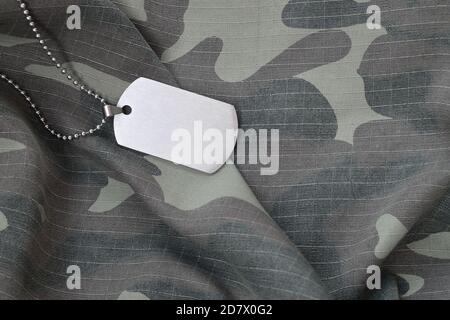 Silvery military beads with dog tag on camouflage fatigue uniform. Army token on soldiers camo jacket rear part Stock Photo