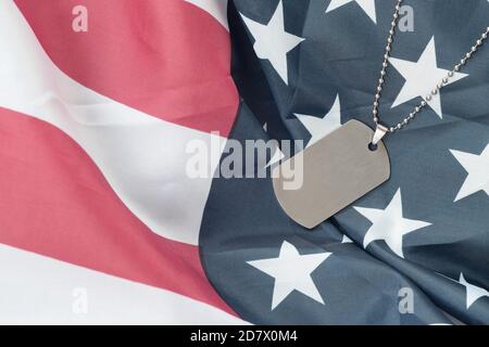 Silvery military beads with dog tag on United States fabric flag. Army token on USA banner close up. Veterans day concept Stock Photo