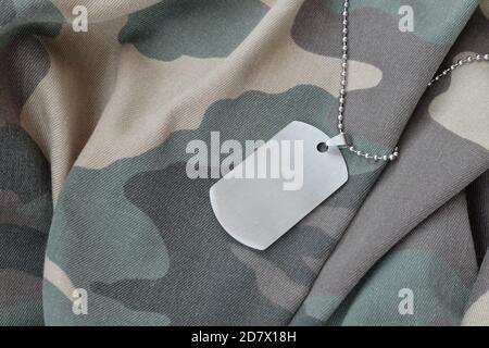 Silvery military beads with dog tag on camouflage fatigue uniform. Army token on soldiers camo jacket rear part Stock Photo