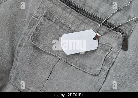 Silvery military beads with dog tag on dark grey vest with pockets. Army token on soldiers camo jacket Stock Photo