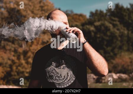 Split Croatia October 2020 Bald bearded man wearing a Game of thrones black shirt taking a sip of beer from a can, thick white vaping smoke leaving th Stock Photo