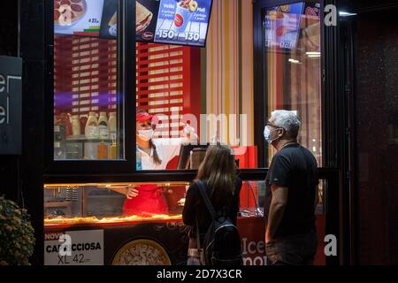 BELGRADE, SERBIA - OCTOBER 6, 2020: Female staff of a take away pizzeria serving clients pizza out of a restaurant wearing a respiratory face mask in Stock Photo