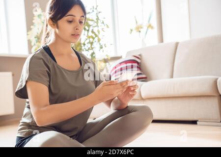 Indian woman holding smart phone using fitness application at home. Stock Photo