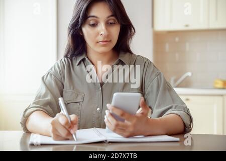 Indian female student holding phone using mobile app learning at home. Stock Photo