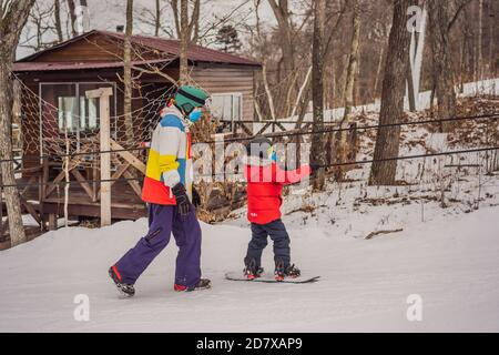 Snowboard instructor teaches a boy to snowboarding wear medical masks due to the COVID-19 coronavirus. Activities for children in winter. Children's Stock Photo