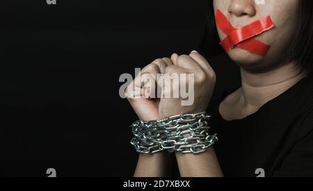 Asian woman blindfold wrapping mouth with red adhesive tape and she was hand tethered interpreter chain black background. Freedom speech censorship an Stock Photo