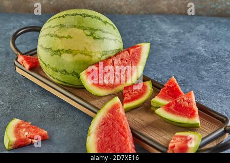 Mini Watermelon with sliced wedges on a wooden stand on a blue background. Stock Photo