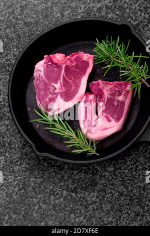 Lamb loin chops with rosemary in a cast iron frying pan.  On a black granite background Stock Photo