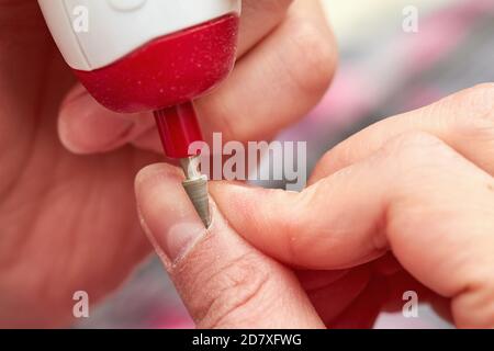 Woman filings nails with electric nail file at home. Electric Nail File Manicure Pedicure Drill. Manicure at home. Closeup, selective focus Stock Photo