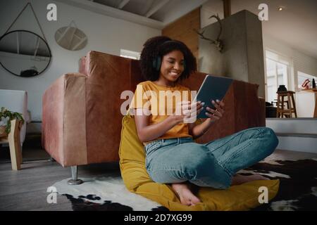 Low angle view of cheerful young woman watching video while relaxing at home using digital tablet with headphones Stock Photo