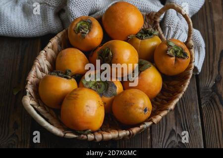 basket with a harvest of persimmons on a wooden table. Country style Stock Photo