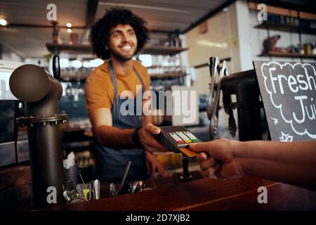 Waiter holding credit card swipe machine while customer typing code in modern cafe Stock Photo