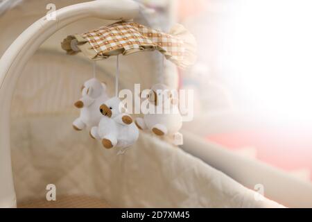 Newborn baby hanging toy, white teddy bears on a checkered beige blanket, baby cradle close-up, copy space background solar flare Stock Photo