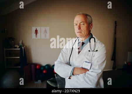 Portrait of serious matured male doctor with crossed arms and stethoscope in labcoat looking at camera Stock Photo