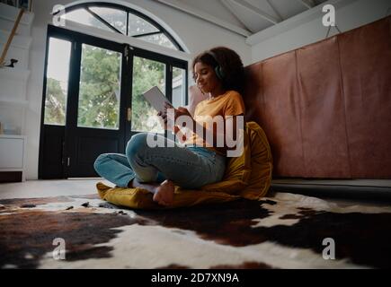 Low angle view of happy woman on carpet watching video on digital tablet and listening to music on headphones Stock Photo