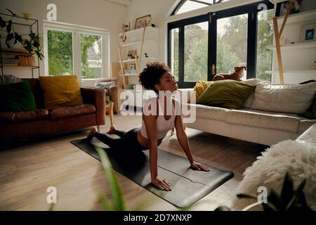 African woman lying on yoga mat at home doing stretching exercise Stock Photo
