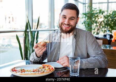 Portrait Happy smiling caucasian man eating Italian pizza in pizzeria keeps social distance. Delicious pizza in cafe. Stock Photo