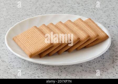 Rectangular shortbread cookies and chocolates in a white plate on a marble top. Stock Photo
