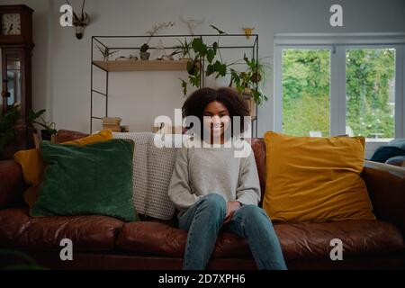 Portrait of beautiful woman with curly hair sitting on couch with cushion