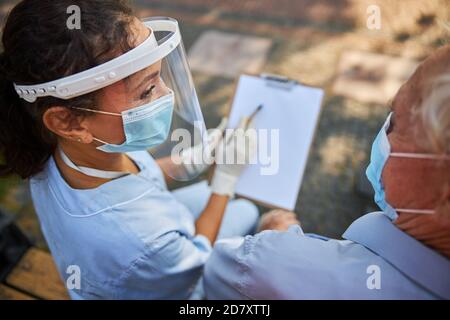 Female nurse in mask and ptotection looking at old patient Stock Photo