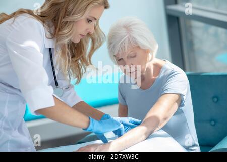 Long-haired smiling nurse making injection to an elderly woman Stock Photo