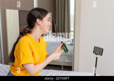 Portrait of young pretty female vlogger streaming live video on smartphone and sshowing a new cosmetic. Side view. Stock Photo