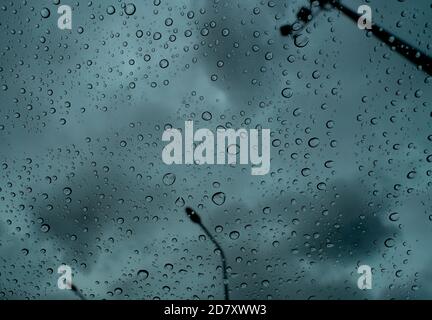Raindrops on transparent glass against blur dark stormy sky and electric pole. Rain drops on windshield. Windshield window of car with raindrops. Stock Photo