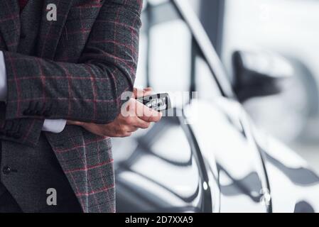 Man in modern formal clothes stands against black car with keys in hand Stock Photo