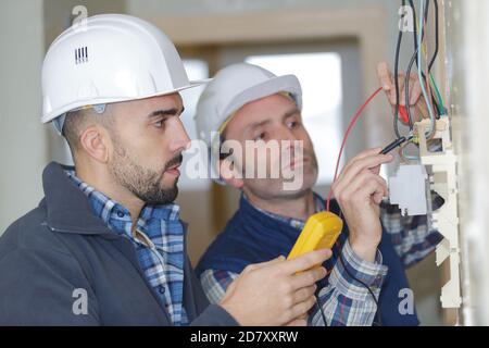 electricians checking socket voltage with digital multimeter two workers Stock Photo