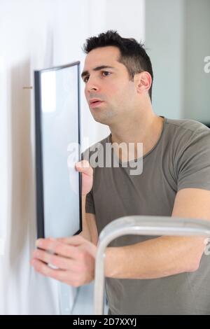 repairman putting picture frame onto wall Stock Photo