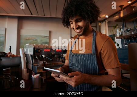 Young man in apron using digital tablet at his cafe Stock Photo