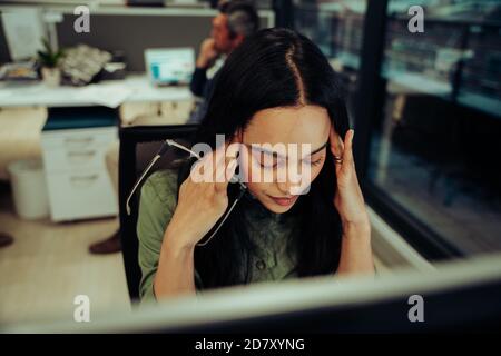 Portrait of stressed female entrepreneur feeling anxious and tired due to work load, sitting with headache in the office Stock Photo