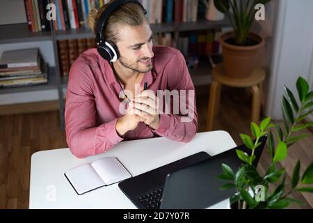 Handsome young caucasian man using computer working at home and talking with headphones feeling happy with smile showing teeth Stock Photo