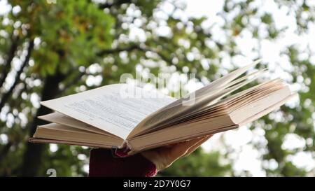 Female hand holding open book with sunlight as concept of freedom of knowledge on green bokeh background in park outdoors. Open book on nature abstrac Stock Photo