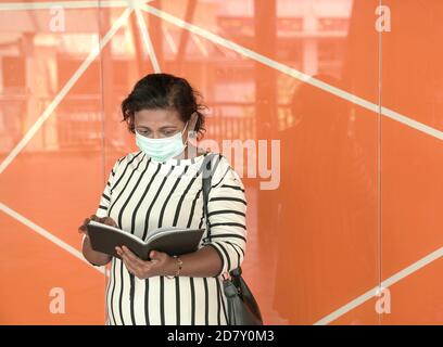Portrait of businesswoman wearing face mask, looking at her diary. Orange background. Stock Photo