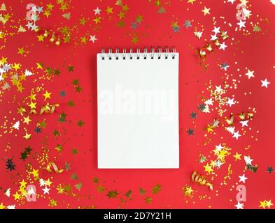 White blank sheet of notebook on a red background with scattered confetti. Holiday education concept. Stock photo. Stock Photo