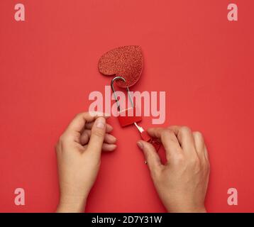 two female hands hold a metal lock and keys on a red background, top view Stock Photo