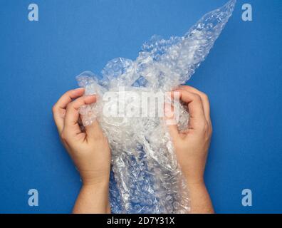 female hand holding crumpled piece of polyethylene with air bubbles on a blue background, packing material Stock Photo