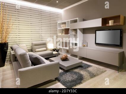 Modern minimalist living room or den interior with beige decor and a large comfortable sofa facing a television and wall unit with coffee table and ru Stock Photo
