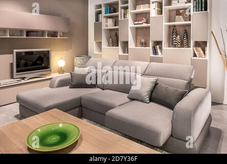 Large comfortable beige sofa in a cozy living room interior with television and wall display unit viewed over a coffe table with green earthenware pla Stock Photo