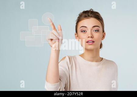 young beautiful woman pressing modern button on virtual screen and looking at the camera on blue background. Stock Photo