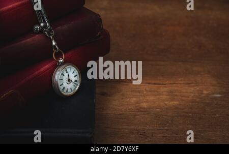 old books stacked up on table with pocket watch  ,moody with room for text ,concept of time passsing . Stock Photo