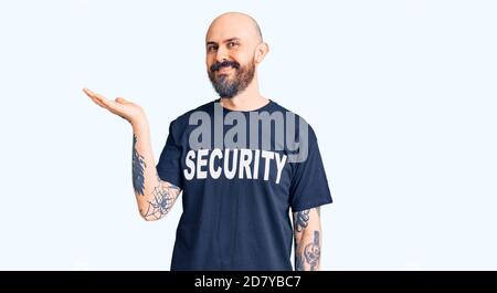 Young handsome man wearing security t shirt smiling cheerful presenting and pointing with palm of hand looking at the camera. Stock Photo