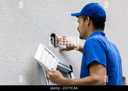 man in blue uniform standing on ladder outdoors and doing maintenance for house ventilation system Stock Photo