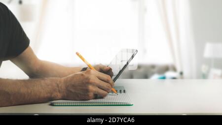 man using digital tablet and writing in note book at home. online learning, distance education and studying concept Stock Photo