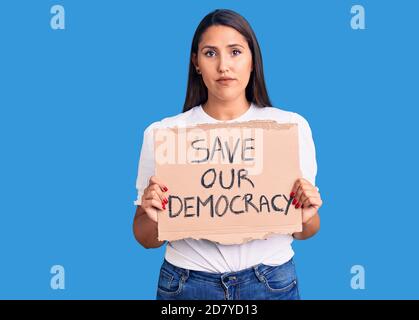 Young beautiful woman holding save our democracy cardboard banner thinking attitude and sober expression looking self confident Stock Photo